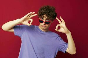 guy with red curly hair guy in a purple t-shirt with sunglasses posing red background photo