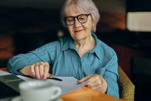 Beautiful mature senior woman with glasses sits at a table in front of a laptop Social networks unaltered photo