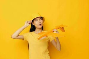 encantador joven asiático mujer en un sombrero con un avión en su manos modelo juguete amarillo antecedentes inalterado foto