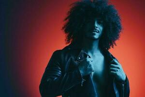 Portrait of fashion man with curly hair on red background multinational, colored light, black leather jacket trend, modern concept. photo