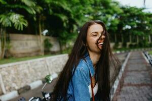 retrato de un mujer morena sonrisa con dientes caminando fuera de en contra un fondo de palma arboles en el zona tropical, verano vacaciones y al aire libre recreación, el despreocupado estilo de vida de un Lanza libre alumno. foto