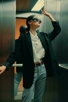 Stylish woman in black jacket and sunglasses posing in elevator, fashion model photo