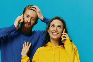 mujer y hombre alegre Pareja con Los telefonos en su manos torcido sonrisa alegre, en azul antecedentes. el concepto de real familia relaciones, hablando en el teléfono, trabajo en línea. foto