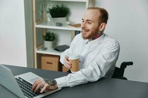 A man in a wheelchair, a businessman with tattoos in the office at a laptop, a coffee break, the concept of working a person with disabilities, freedom from social frames photo