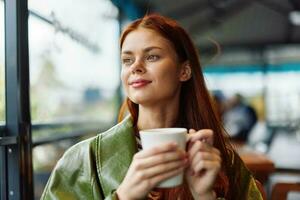 Portrait of a woman influencer drinking a drink from a mug in a cafe and smiling looking out the window, content blogger close-up photo