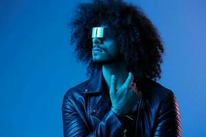 Portrait of fashion man with curly hair with stylish glasses on blue background multinational, colored light, black leather jacket trend, modern concept. photo