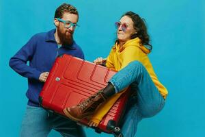 Woman and man smile suitcases in hand with yellow and red suitcase smile fun, on blue background, packing for a trip, family vacation trip. photo