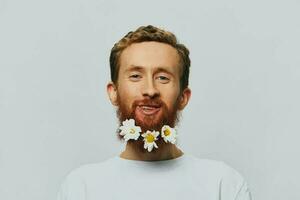 Portrait of a funny man in a white T-shirt with flowers daisies in his beard on a white isolated background, copy place. Holiday concept and congratulations. photo