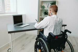 man wheelchair businessman with tattoos in the office works at a laptop online, business process from the back, copy space, integration into society, the concept of working a person with disabilities photo