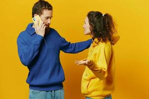 Man and woman couple with phone in hand call talking on the phone, on a yellow background, symbols signs and hand gestures, family quarrel jealousy and scandal. photo