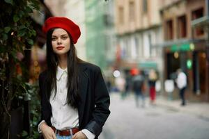 mujer Moda modelo soportes en el calle en el ciudad entre el multitud en un chaqueta y rojo boina y vaqueros, cinematográfico francés Moda estilo ropa, viaje a Estanbul foto