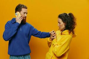 Woman man cheerful couple with phones in hand social networking and communication crooked smile fun and fight, in yellow background. The concept of real family relationships, freelancers, work online. photo