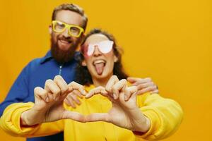 Man and woman couple smiling cheerfully and crooked with glasses, on yellow background, symbols signs and hand gestures, family shoot, newlyweds. photo