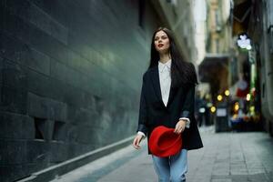 Fashion woman tourist in stylish clothes in a jacket and red beret walking down a narrow city street flying hair and happy travel, French style, cinematic color, retro style. photo