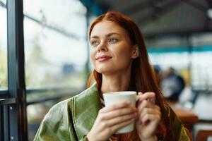 Portrait of a woman influencer drinking a drink from a mug in a cafe and smiling looking out the window, content blogger close-up photo