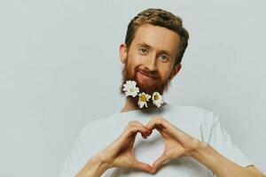 Portrait of a funny man in a white T-shirt with flowers daisies in his beard on a white isolated background, copy place. Holiday concept and congratulations. photo