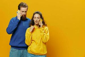 Man and woman couple smiling merrily with phone in hand social media viewing photos and videos, on yellow background, symbols signs and hand gestures, family freelancers.