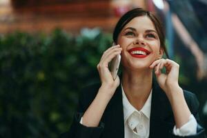 Woman blogger tourist sits in a cafe at a table with a phone in her hands conversation, mobile communication and internet in spring travel, video business call, freelance work online, smile with teeth photo