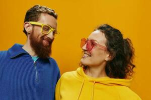 Man and woman couple smiling cheerfully and crooked with glasses, on yellow background, symbols signs and hand gestures, family shoot, newlyweds. photo