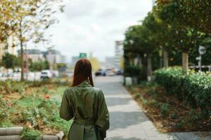 un mujer camina alrededor el ciudad desde detrás en un elegante impermeable foto