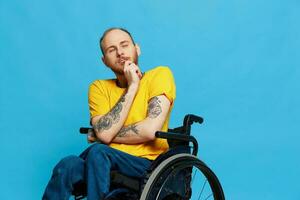 un hombre se sienta en un silla de ruedas consideración en un camiseta en un azul antecedentes en el estudio, el concepto de un gratis sin barreras ambiente para personas con discapacidades foto