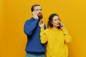 Woman and man cheerful couple with phones in hand talking on cell phone crooked smile cheerful, on yellow background. The concept of real family relationships, talking on the phone, work online. photo