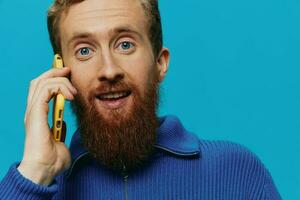 Portrait of a man with a phone in his hands talking, calling, on a blue background. Communicating online social media, lifestyle photo