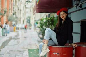 A beautiful woman smiling with teeth stands outside a cafe on a city street, a stylish fashion look of clothes, vacation and travel. photo