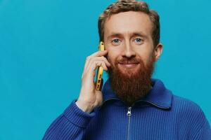 Portrait of a man with a phone in his hands talking, calling, on a blue background. Communicating online social media, lifestyle photo