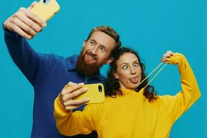 Woman and man funny couple with phones in hand taking selfies crooked smile fun, on blue background. The concept of real family relationships, talking on the phone, work online. photo