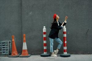 Fashion woman standing leaning against a wall street against a background of the city road works tourist in stylish clothes with red lips and red beret, travel, cinematic color, retro vintage style. photo