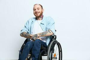 A man in a wheelchair and pointing a finger at, copy space, with tattoos on his hands sits on a gray studio background, health concept a person with disabilities, a real person photo