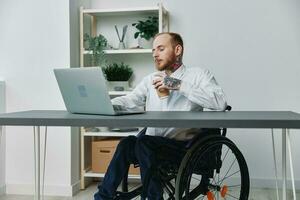 un hombre en un silla de ruedas un empresario con tatuajes en el oficina trabajos a un ordenador portátil con café, integración dentro sociedad, el concepto de trabajando un persona con discapacidades, libertad desde social marco de referencia foto