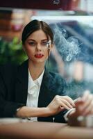 elegante mujer se sienta en un café a un mesa y fuma un cigarrillo, un malo hábito foto