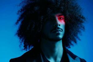 Fashion portrait of a man with curly hair on a blue background with a red stripe of light, multicolored light, trendy, modern concept. photo