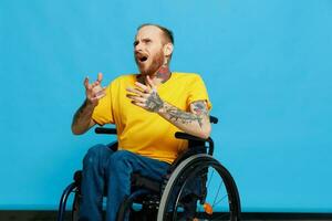 un hombre en un silla de ruedas en un camiseta con tatuajes en su brazos se sienta en un azul estudio fondo, un lleno vida, un real persona foto