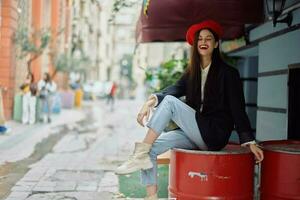 un hermosa mujer sonriente con dientes soportes fuera de un café en un ciudad calle, un elegante Moda Mira de ropa, vacaciones y viajar. foto