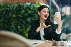 Stylish woman blogger tourist sits in a cafe with a phone in her hands reads a message, mobile communication and internet on a journey, video call, freelance work online, smile with teeth photo
