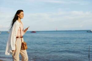 Freelance woman with phone in hand on vacation walking on the beach by the ocean in Bali, happy travel and vacation, mobile communication photo