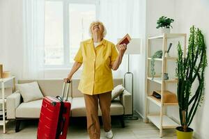 Happy senior woman with passport and travel ticket packed a red suitcase, vacation and health care. photo