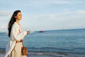 Freelance woman with phone in hand on vacation walking on the beach by the ocean in Bali, happy travel and vacation, mobile communications, Internet online photo