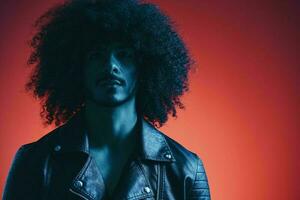 Portrait of fashion man with curly hair on red background multinational, colored light, black leather jacket trend, modern concept. photo