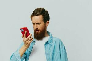 Man hipster with phone in hand blogger smile on gray background in blue shirt and white t-shirt, talking on the phone and selfies photo