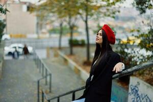 Fashion woman walking down steps against city backdrop in stylish clothes with red lips and red beret, travel, cinematic color, retro vintage style, urban fashion lifestyle. photo