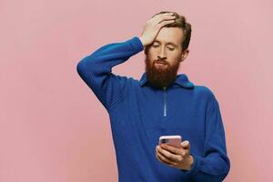 Portrait of a man with a phone in his hands doing looking at it and talking on the phone, on a pink background. Communicating online social media, lifestyle photo