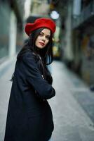 Moda mujer retrato caminando turista en elegante ropa con rojo labios caminando abajo estrecho ciudad calle, viajar, cinematográfico color, retro Clásico estilo, dramático Mira sin sonrisa tristeza. foto