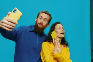 Woman and man funny couple with phones in hand taking selfies crooked smile fun, on blue background. The concept of real family relationships, talking on the phone, work online. photo