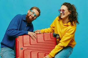 mujer y hombre sonrisa maletas en mano con amarillo y rojo maleta sonrisa divertido, en azul fondo, embalaje para un viaje, familia vacaciones viaje. foto