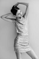 Black and white photo of a woman in a stylish sequined party dress posing near a wall