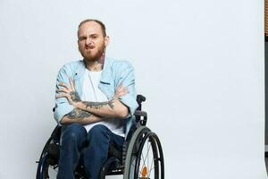 A man in a wheelchair looks at the camera anger and aggression, with tattoos on his arms sits on a gray studio background, health concept man with disabilities photo